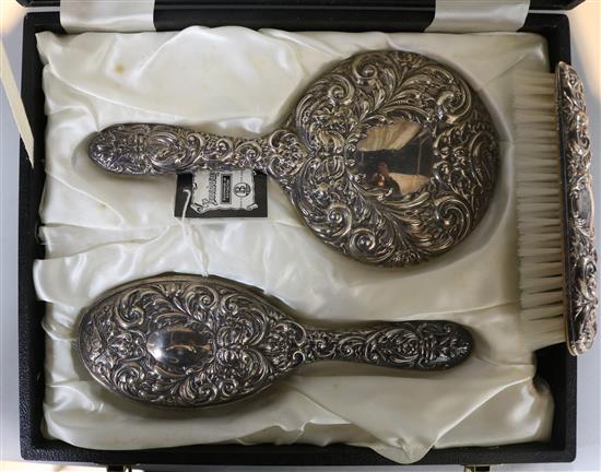 A cased repousse silver three piece brush set.